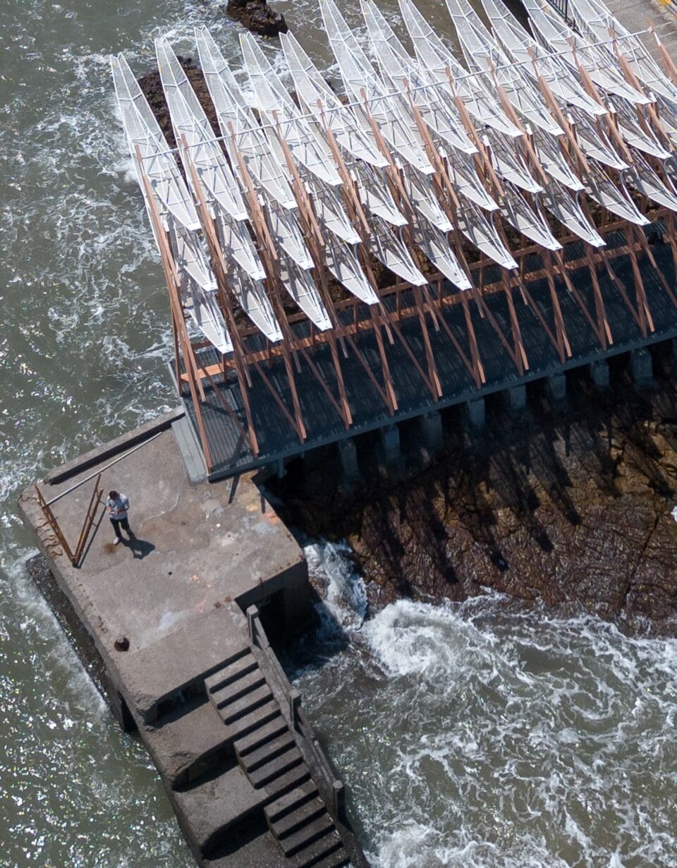 an aerial view of a person walking near seaside pavilion made of white feather-like blades