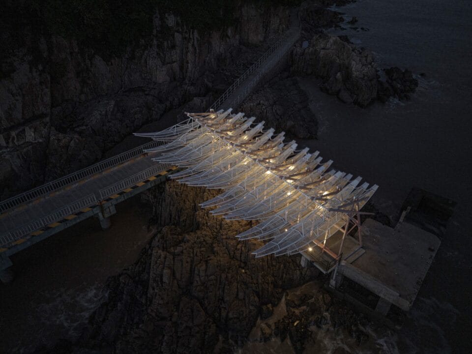 a nighttime aerial view of a seaside pavilion made of white feather-like blades