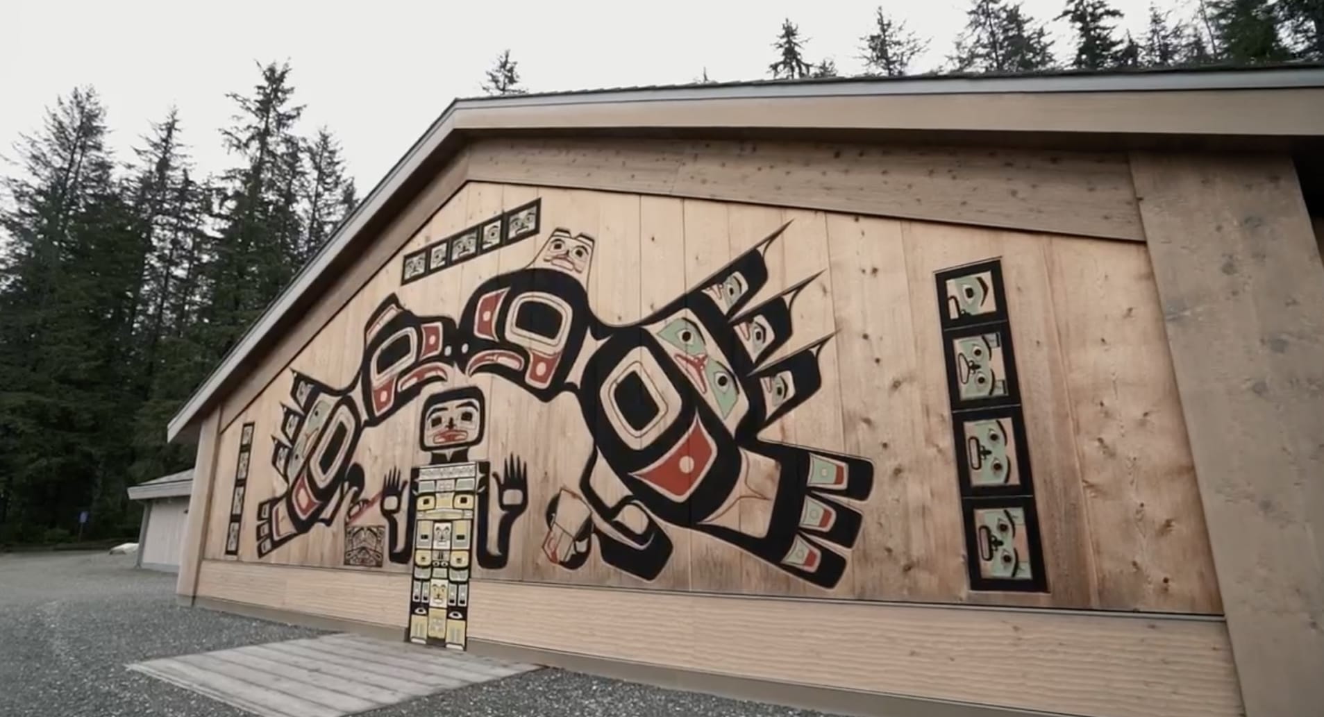 a still from a short film about a Huna Tlingit ancestral tribal house being constructed, showing the outside with numerous hand-carved and painted panels