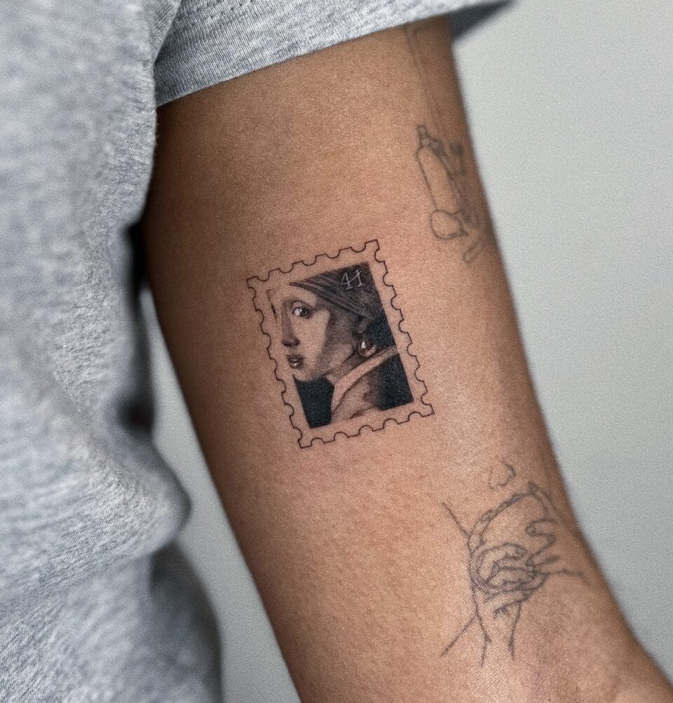 a photograph of a postage stamp-shaped tattoo on the inside of an upper arm, containing a compositional detail of a detail of Vermeer's 'Girl with a Pearl Earring'