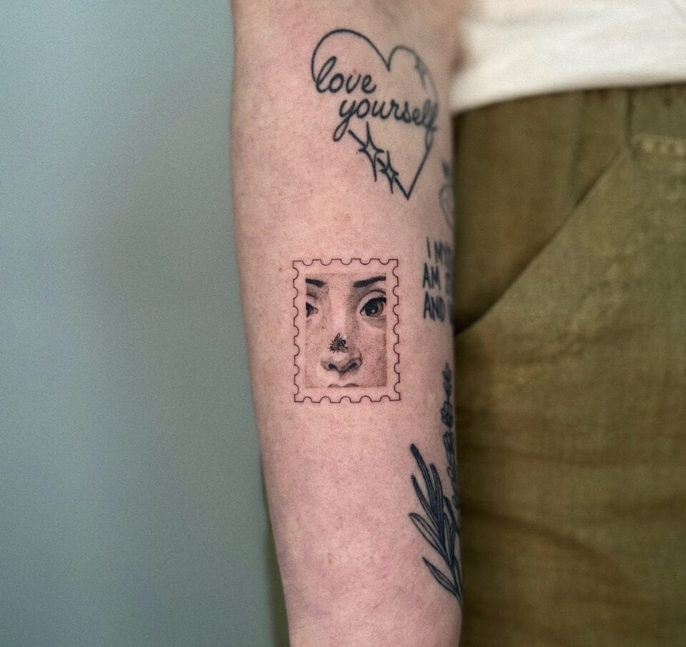 a photograph of a postage stamp-shaped tattoo on a forearm, containing a compositional detail of a detail of a woman's face with a fly on her nose