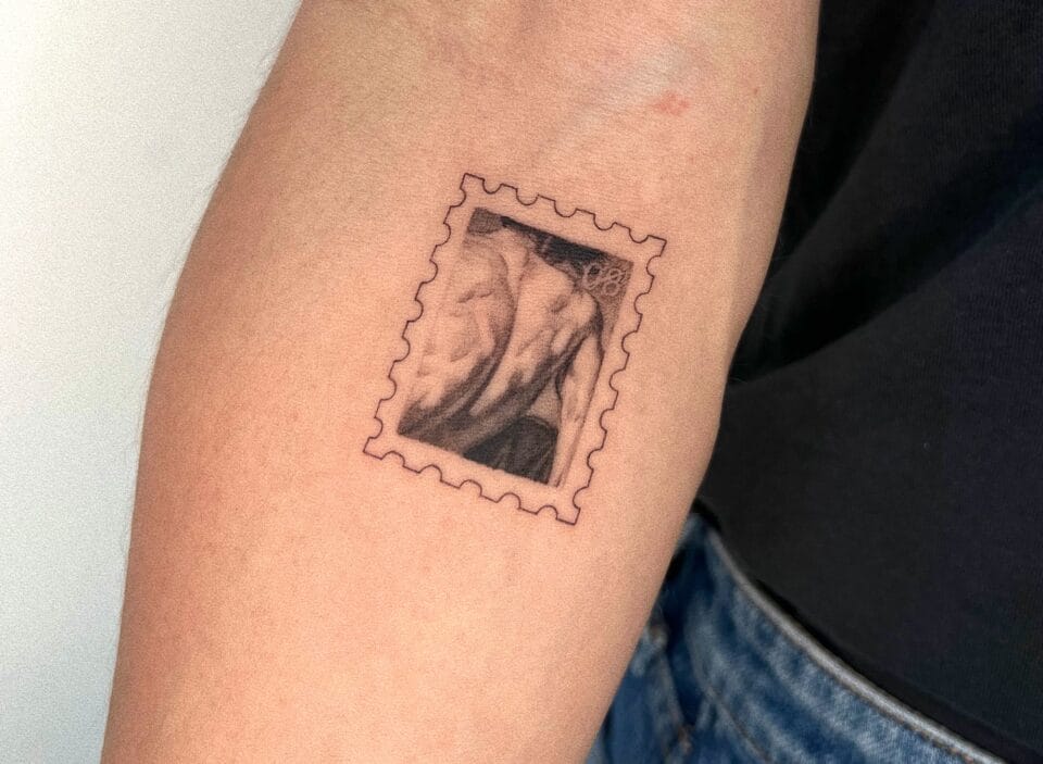 a photograph of a postage stamp-shaped tattoo on a forearm, containing a compositional detail of a muscular back of a male figure evocative of Caravaggio