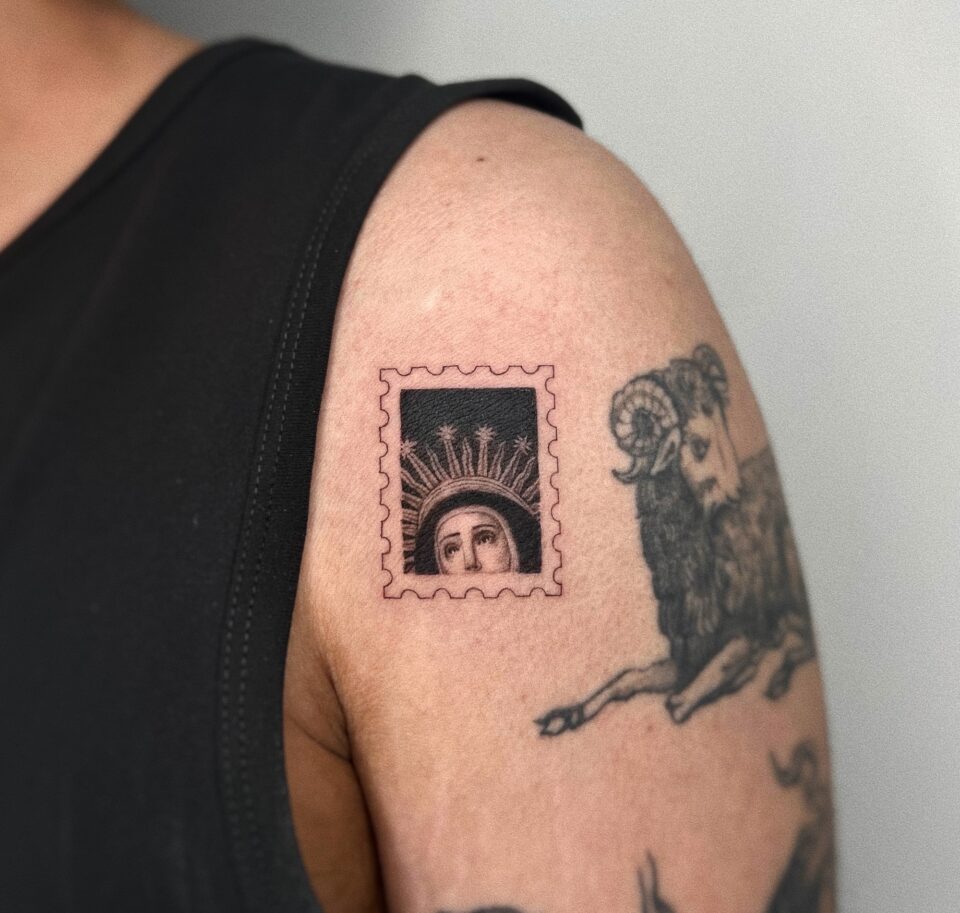 a photograph of a postage stamp-shaped tattoo on a shoulder, containing a compositional detail of the top half of a religion female icon's face
