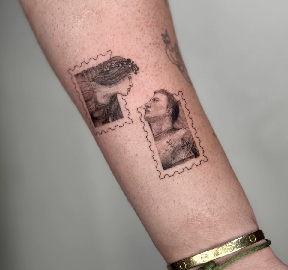 a photograph of two postage stamp-shaped tattoos on a forearm, containing compositional details of a man and woman reaching out of the stamps' frames toward one another