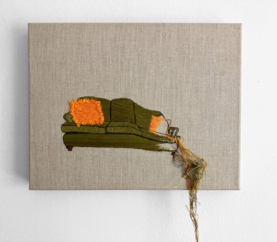 an embroidery of a green couch with orange pillows that's unraveling and spilling off the canvas on the right edge