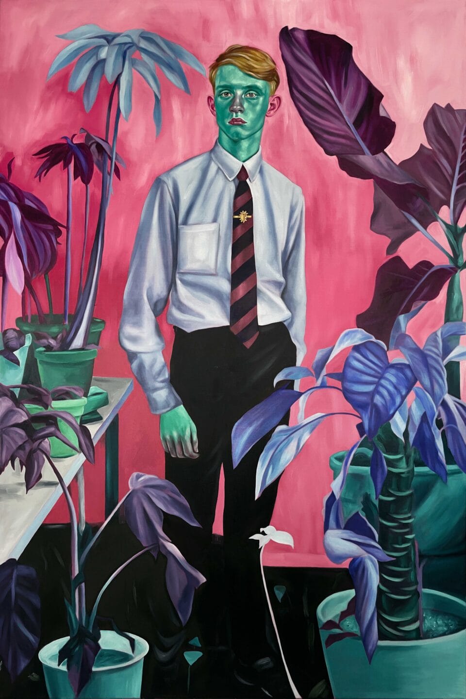 a young man in a white shirt and tie, with a teal-colored face and green hands, stands amid a number of potted plants in an office setting with a pink background