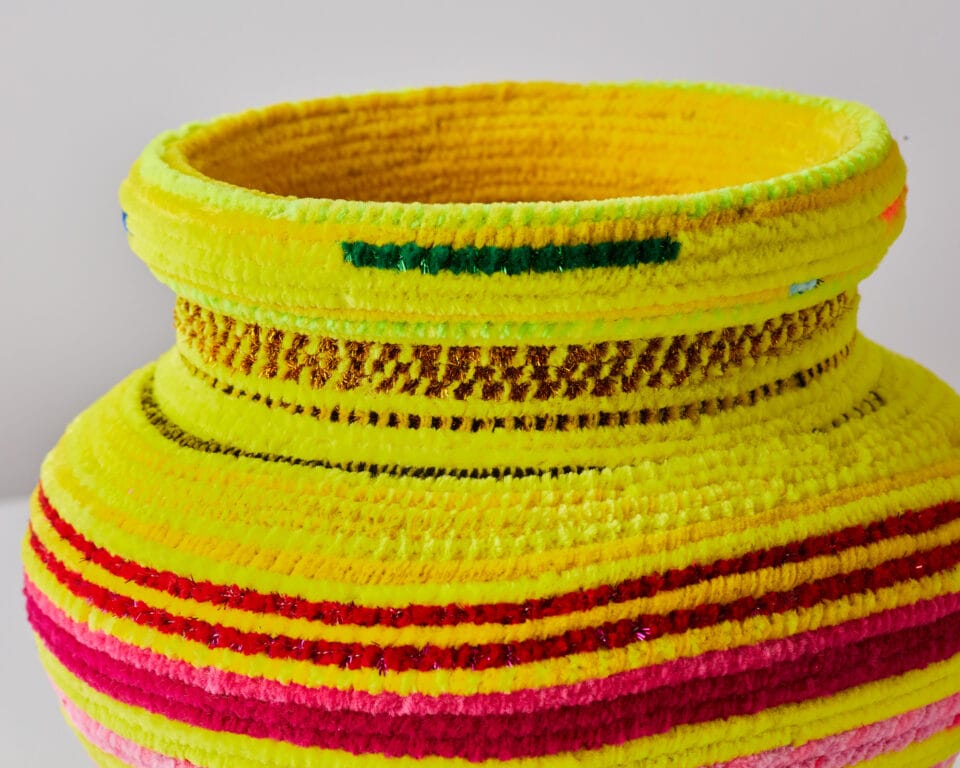 detail of a a vessel made from woven pipe cleaners in shades of yellow and pops of red, pink, and green