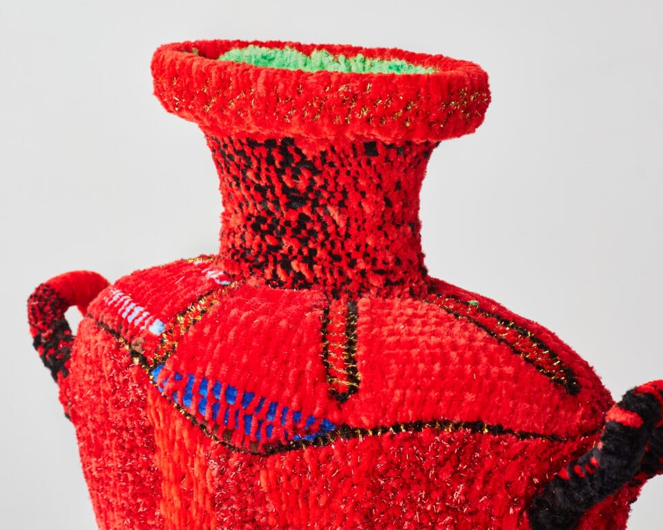 a vessel made from woven pipe cleaners in shades of red with small pops of light green and royal blue