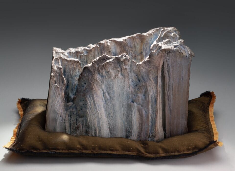 a sculpture made from a set of large books, covers removed to reveal the stitched binding, which has been water-blasted to soften and manipulate the pages into a form resembling a large mountain or glacier