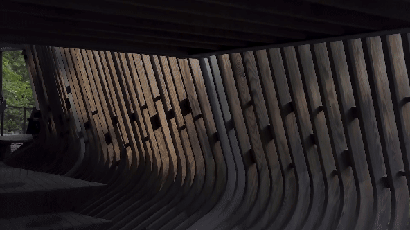 a gif of a drone compilation documenting a contemporary tree house with raised walkways in some woods with the sun shining through the trees