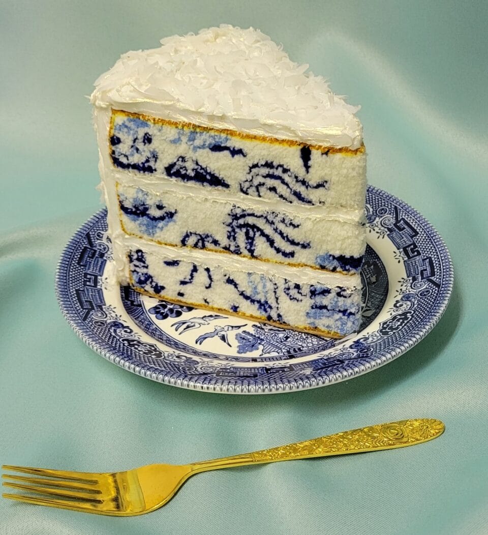a small sculpture of a slice of layer cake sitting on a blue-and-white porcelain plate, with realistic frosting details and embroidery that looks like the texture of fluffy sponge in the pattern of a Delftware plate