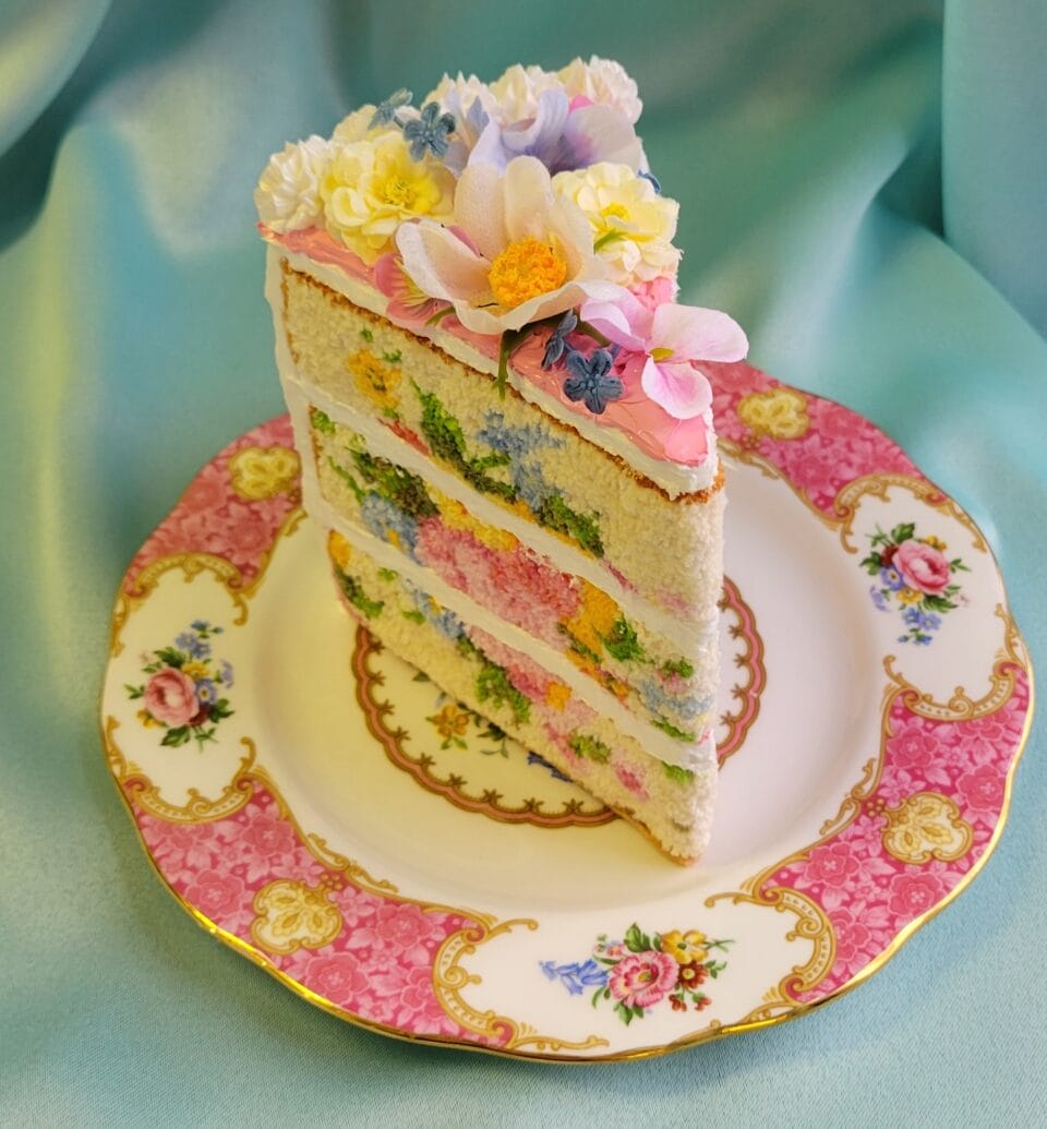 a small sculpture of a slice of layer cake on an ornate pink plate, with realistic frosting details and embroidery on that looks like the texture of fluffy sponge