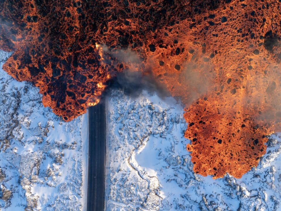 an aerial view of a road through icy terrain with lava moving over it