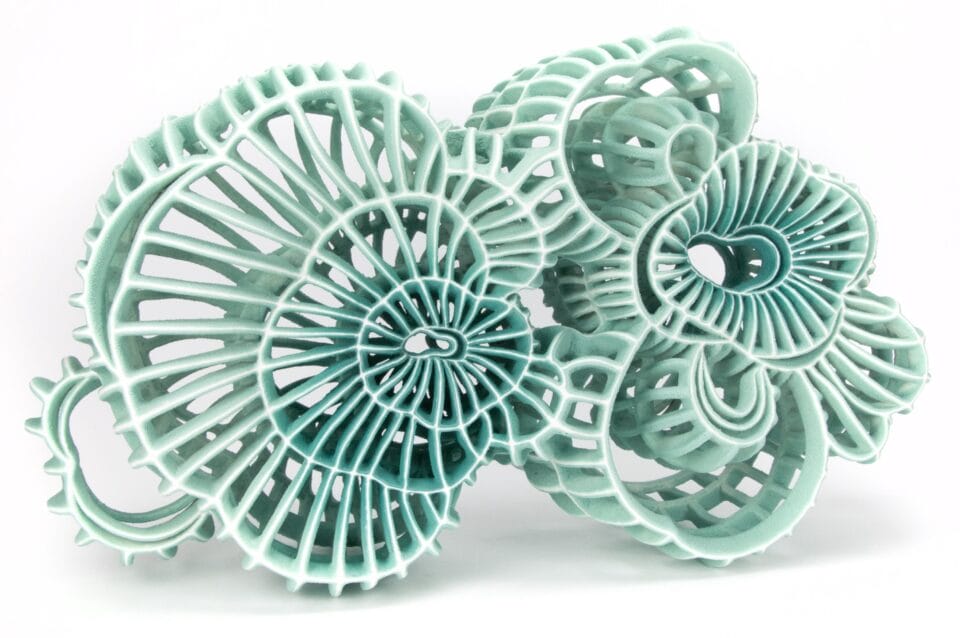 an abstract ceramic sculpture with seafoam green porcelain and white flocked-like surfaces with numerous spokes and irregular concentric circles that mimic the shape of microscopic organisms