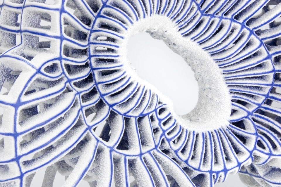 a detail of an abstract ceramic sculpture with blue porcelain and white flocked-like surfaces with numerous spokes and irregular concentric circles and an oval-ish opening