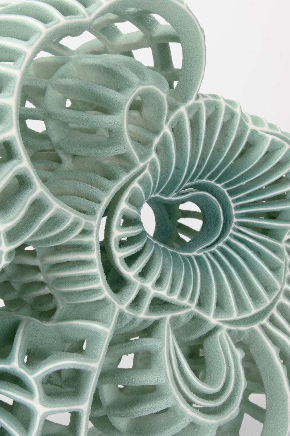 a detail of an abstract ceramic sculpture with seafoam green porcelain and white flocked-like surfaces with numerous spokes and irregular concentric circles that mimic the shape of microscopic organisms