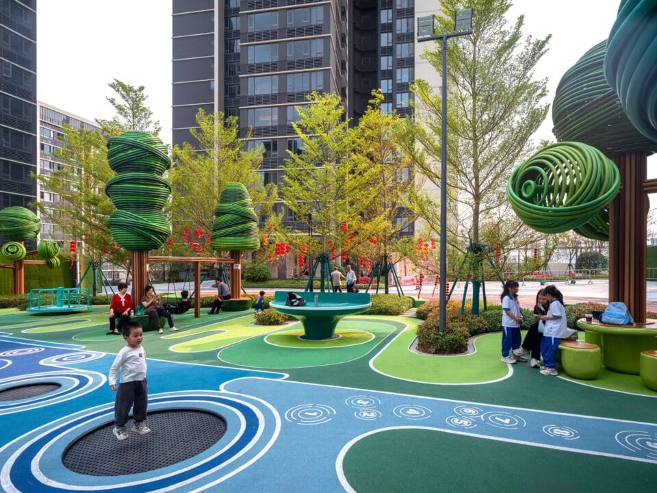 part of an elaborately designed playground with blue and green designs on the ground and wire-like sculptural trees holding up bridges and play equipment