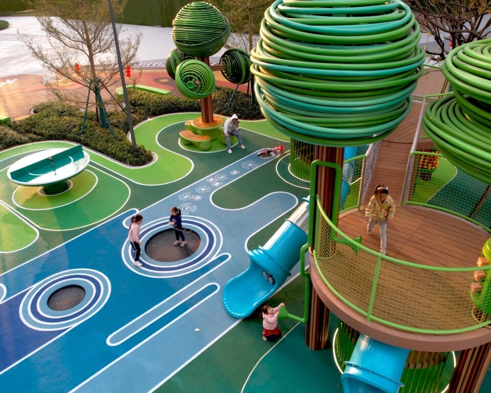 an aerial view of an elaborately designed playground with blue and green designs on the ground and wire-like sculptural trees holding up bridges and play equipment