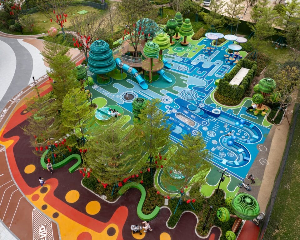 an aerial view of an elaborately designed playground with blue and green designs on the ground and wire-like sculptural trees holding up bridges and play equipment