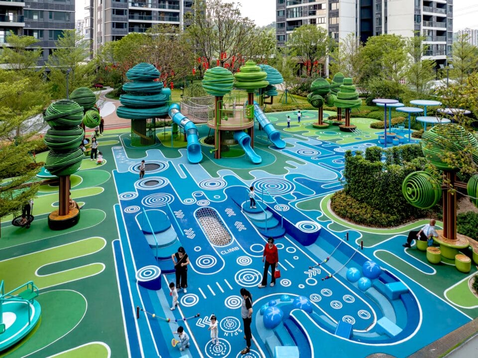 an aerial view of an elaborately designed playground with blue and green designs on the ground and wire-like sculptural trees holding up bridges and play equipment