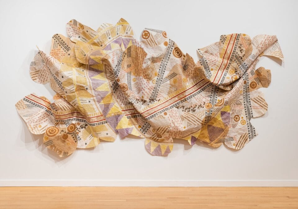 a large, patchwork wall hanging made from kapa, or barkcloth, dyed with numerous natural dyes