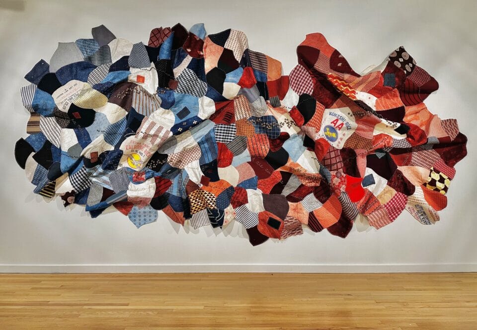 a large, patchwork wall hanging made from kapa, or barkcloth, dyed with numerous natural dyes that turn gradually from blue on the left to red on the right