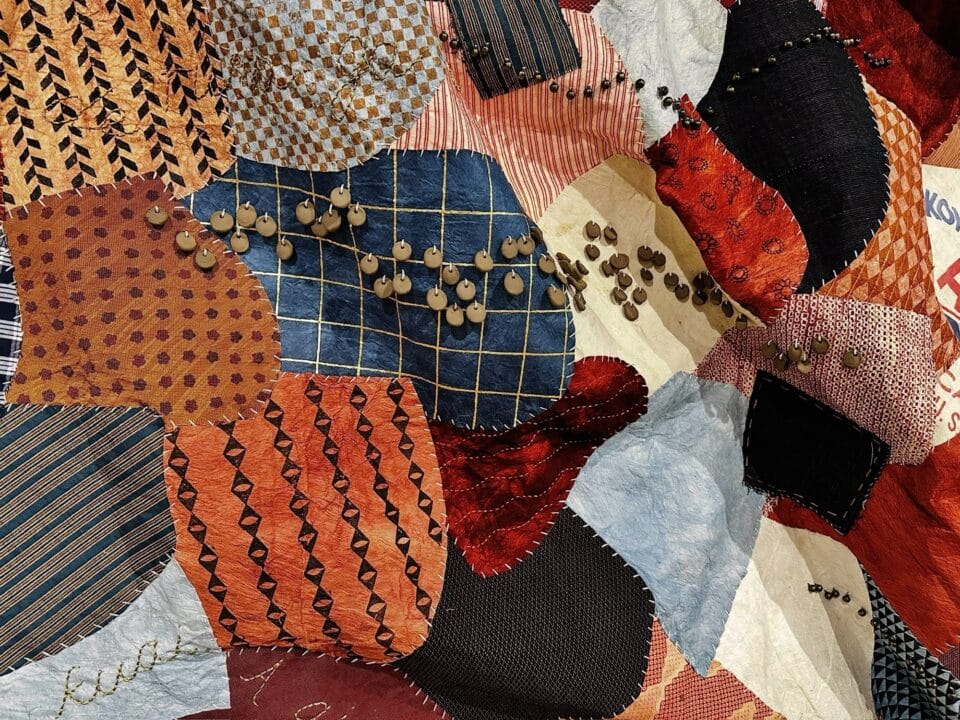 a detail of a large, patchwork wall hanging made from kapa, or barkcloth, dyed with numerous natural dyes