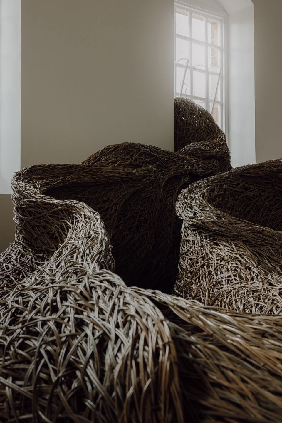 a detail of a sculptural installation that moves through an architectural space and interacts with windows, made of woven willow branches