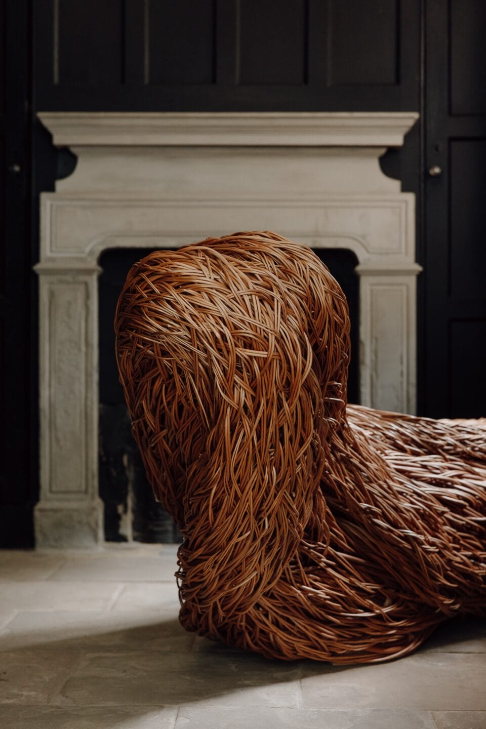 a detail of a sculptural installation that moves through an architectural space, made of woven willow branches