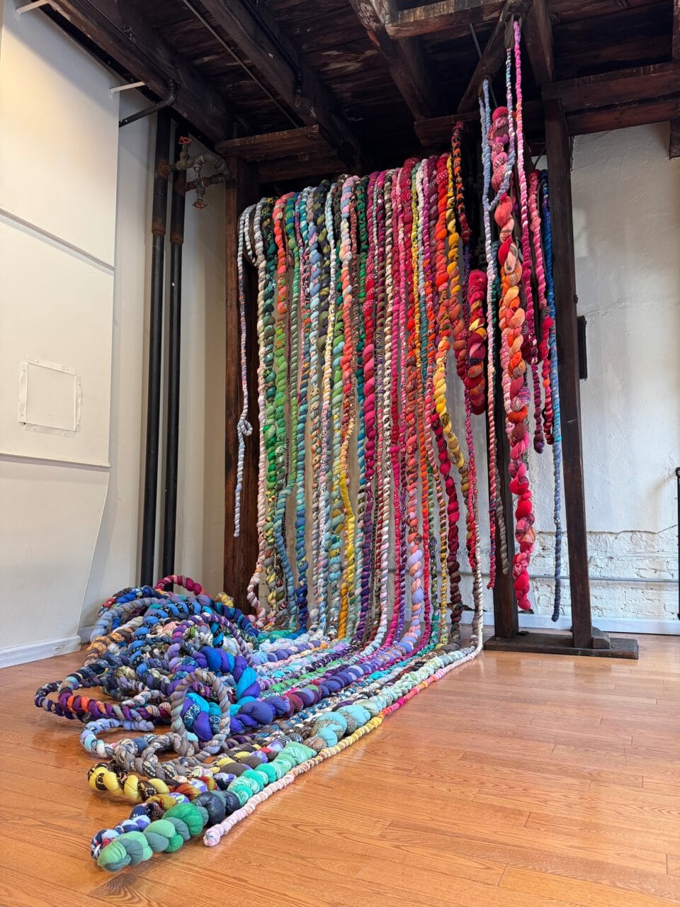 colorful textile strands spill down in a gallery