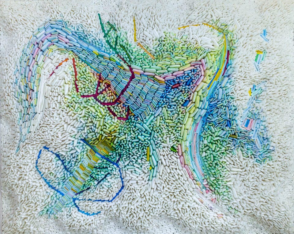 an abstract work of tiny rolled paper seeds with a blue and green section in the center surrounded by white