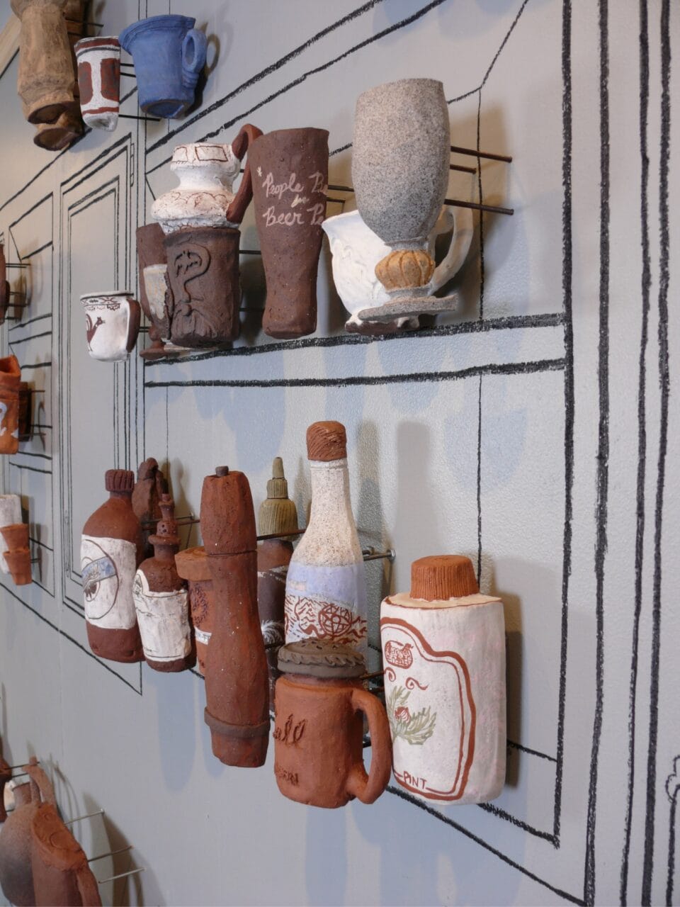 a gallery wall outlined with kitchen cabinets and counters, with three-dimensional reliefs of ceramic vessels and objects installed on the wall