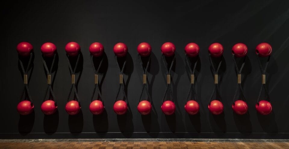a wall installation of several oversized red ball hair ties on a black wall