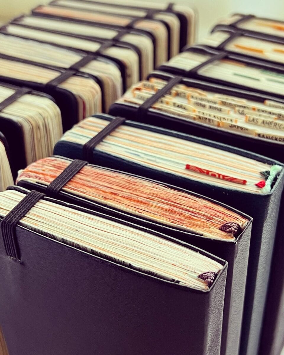 the tops of a series of closed, small sketchbooks showing how full they have become, with color and details on the edges