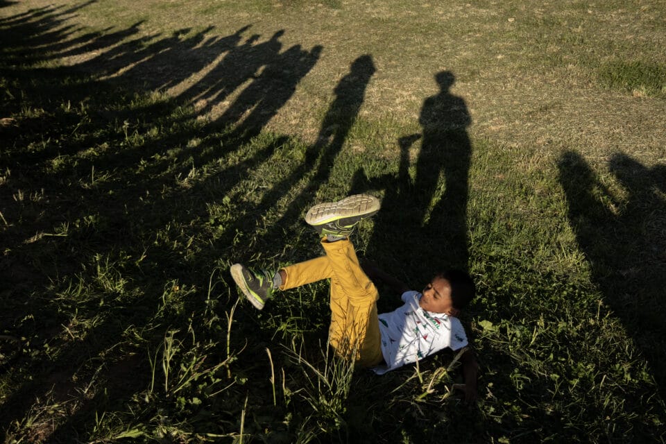a kid in the grass with his legs up is surrounded by dozens of figurative shadows