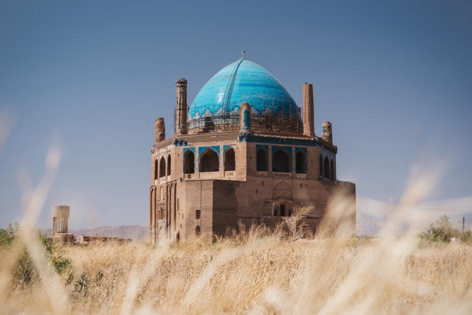 a blue-domed mausoleum against a blue sky in a field of golden grass