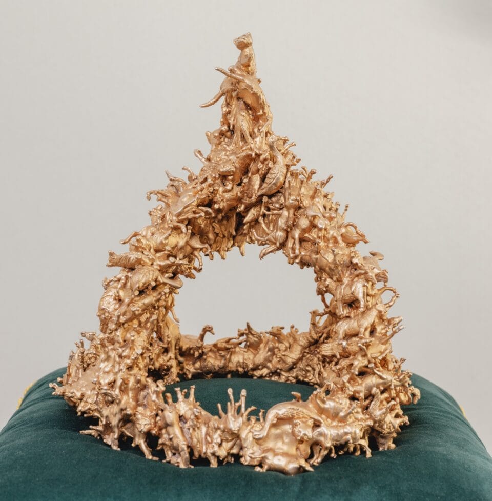 a sculpture of a bronze crown composed of tiny birds and other animals, coated in metallic silver, situated on a green velvet cushion