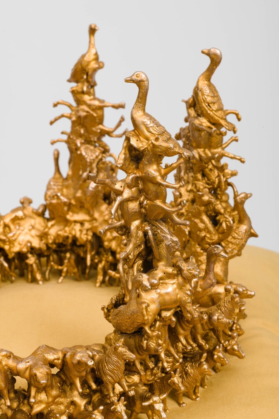 a detail of a sculpture of a gold-coated bronze crown composed of tiny birds and other animals, situated on yellow velvet cushion