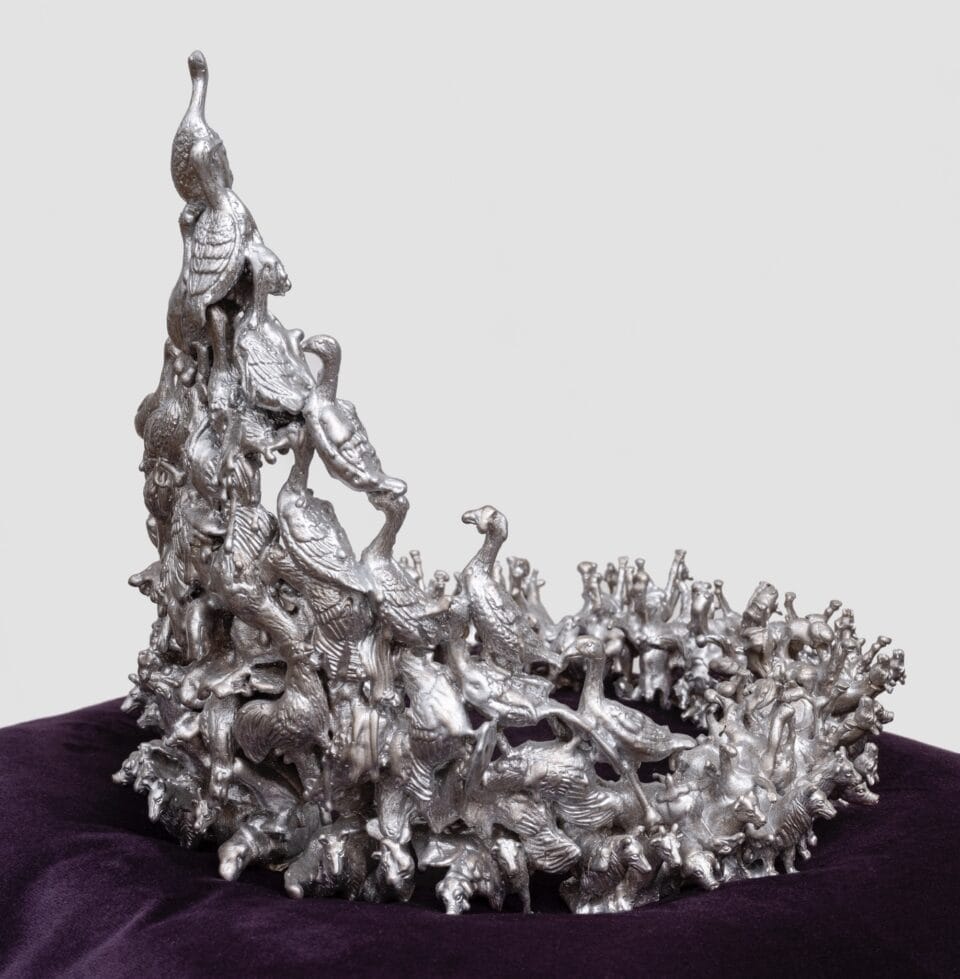 a sculpture of a bronze crown composed of tiny birds, coated in metallic silver, situated on a black velvet cushion