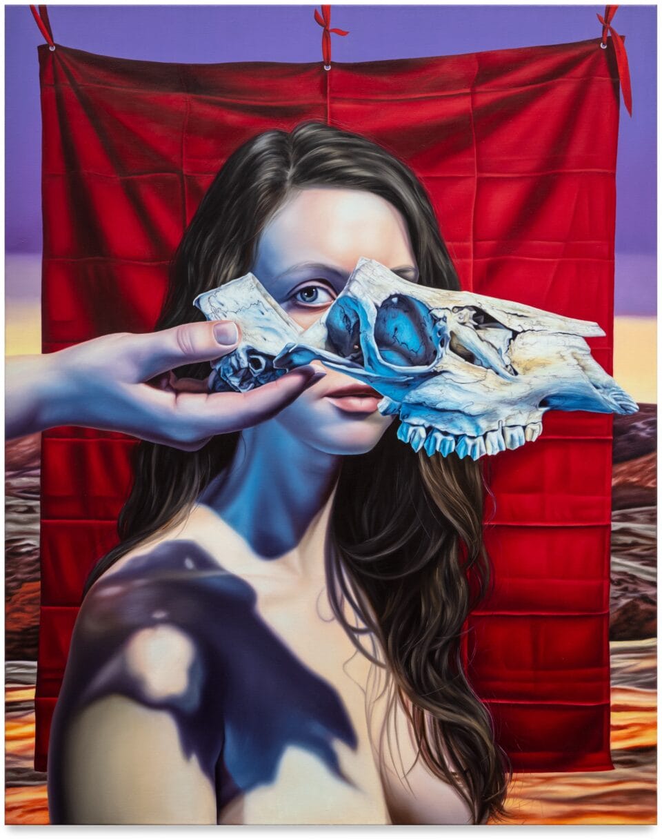 a portrait of a brown-haired woman in front of a red drape, which hangs in front of a Western landscape, with an animal skull being held in front of her eyes