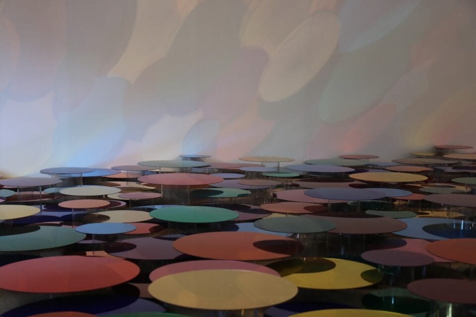 a floor installation of numerous shiny, colorful circles reflecting onto a wall